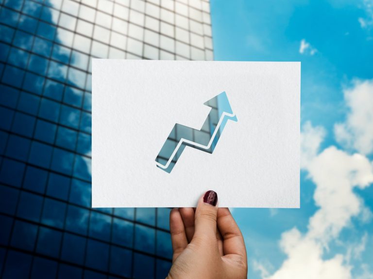 NPL Una mano sostiene un gráfico de tendencia ascendente frente a un edificio moderno.