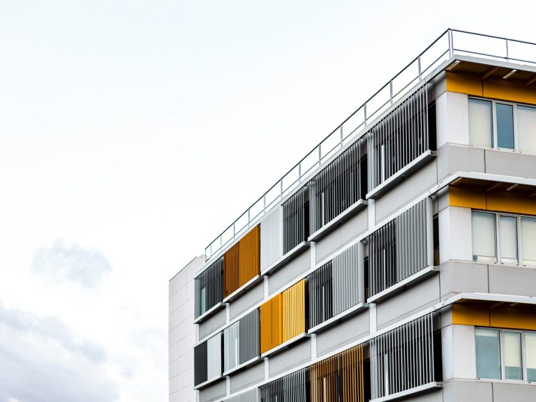 vivienda ocupada Edificio moderno con fachada gris y paneles amarillos y anaranjados. Cielo nublado.